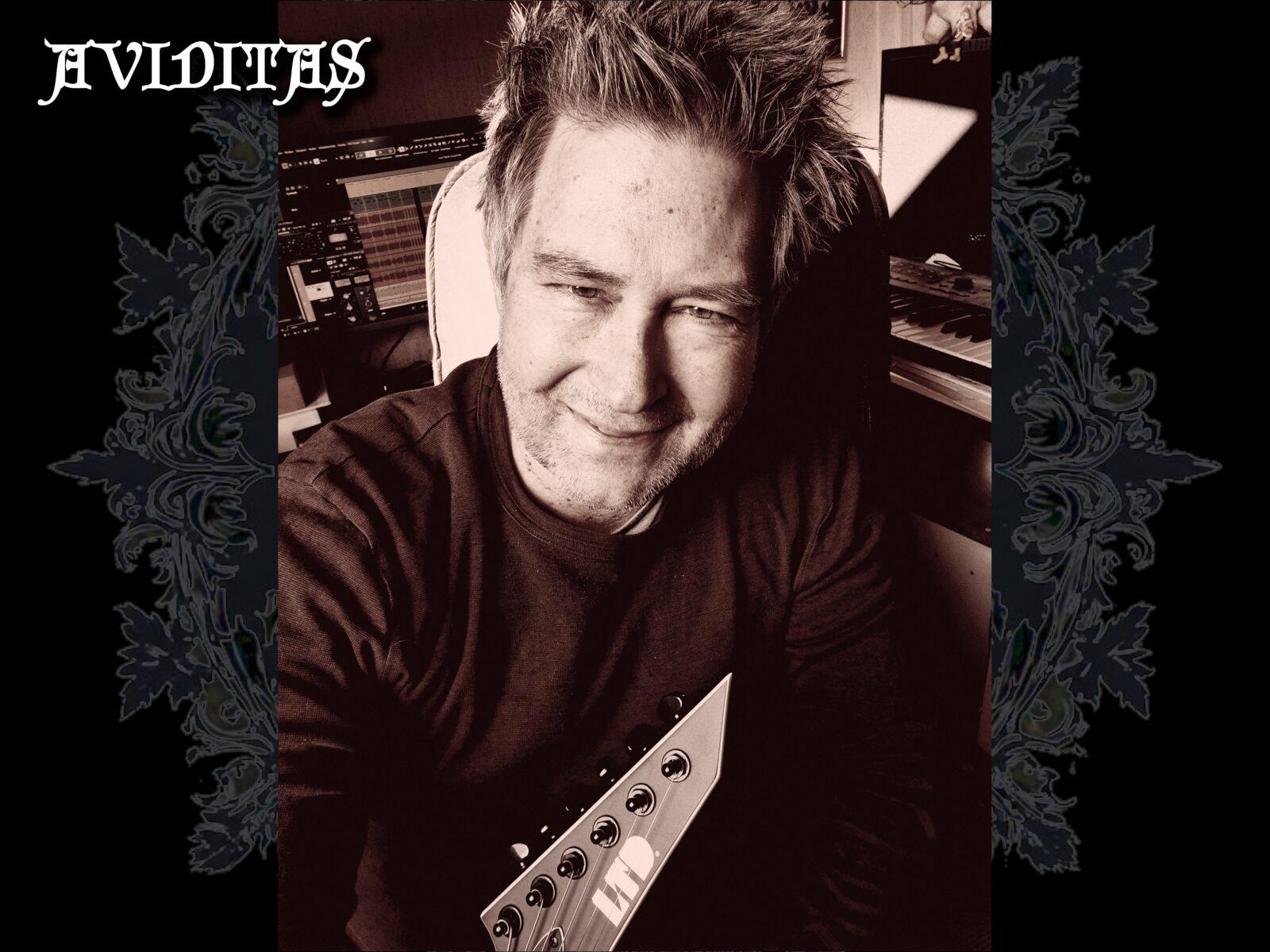 Matt Schneider, do AVIDITAS, no estúdio caseiro ao lado de uma guitarra LTD e um teclado